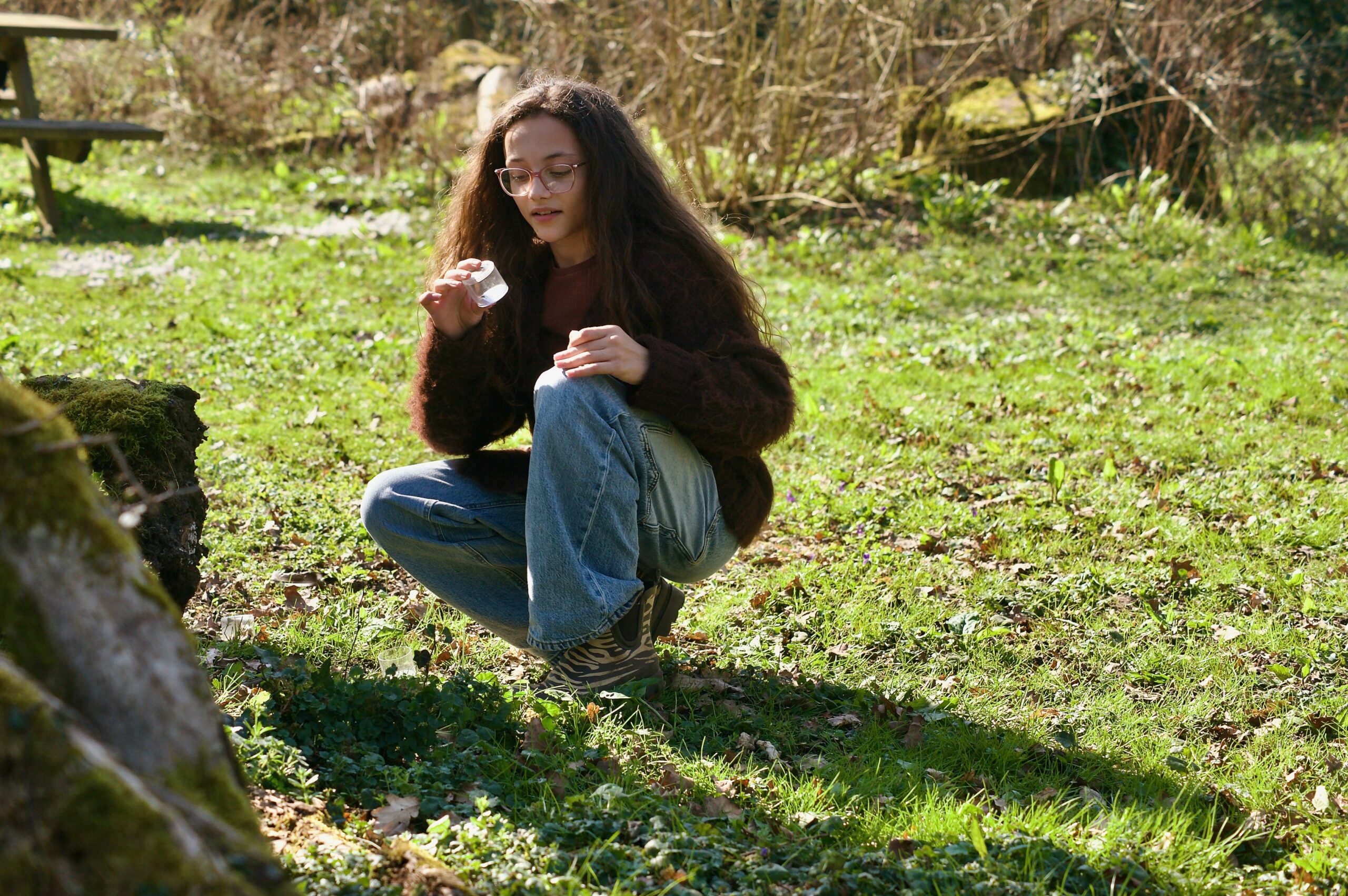 A young girl looks with interest at something she has found in nature.